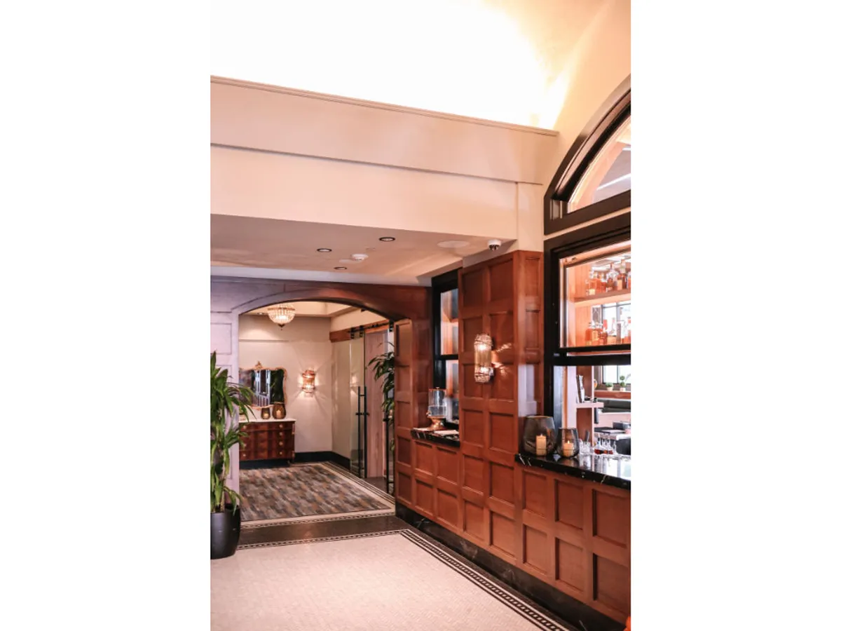An elegant lobby or common area with wood paneling, chandeliers, lush plants, and a comfortable bar space. The setting feels both sophisticated and inviting, ideal for social gatherings, relaxation, or a welcoming first impression.