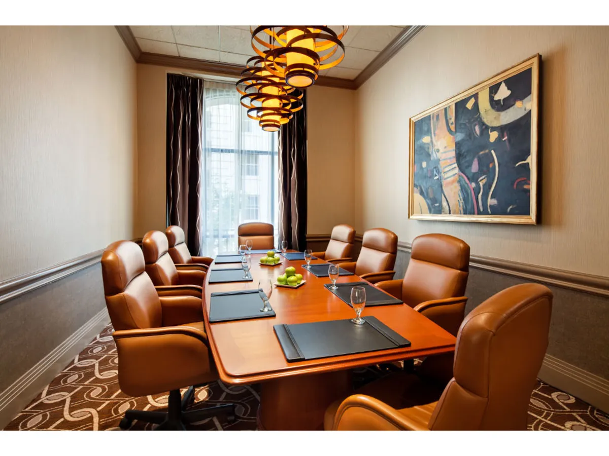 A stylish conference area showcasing a polished wooden table surrounded by leather chairs, modern light fixtures, and artwork on the walls. Glassware is arranged on the table, hinting at an environment suited for both formal business discussions and informal networking.