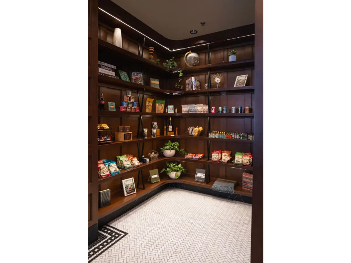 A cozy corner highlighted by wooden shelves filled with snacks, beverages, and decorative plants, set atop intricate patterned flooring. The scene invites moments of refreshment and convenience.