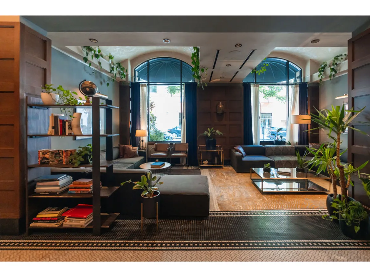 A bright room with large windows, comfortable seating, plants, a bookshelf, and a coffee table, offering an open, inviting layout ideal for relaxation or socializing. The arrangement ensures easy movement and barrier-free access.